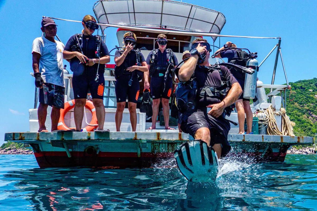 Divemaster candidate striding off the boat platform as the crew looks on