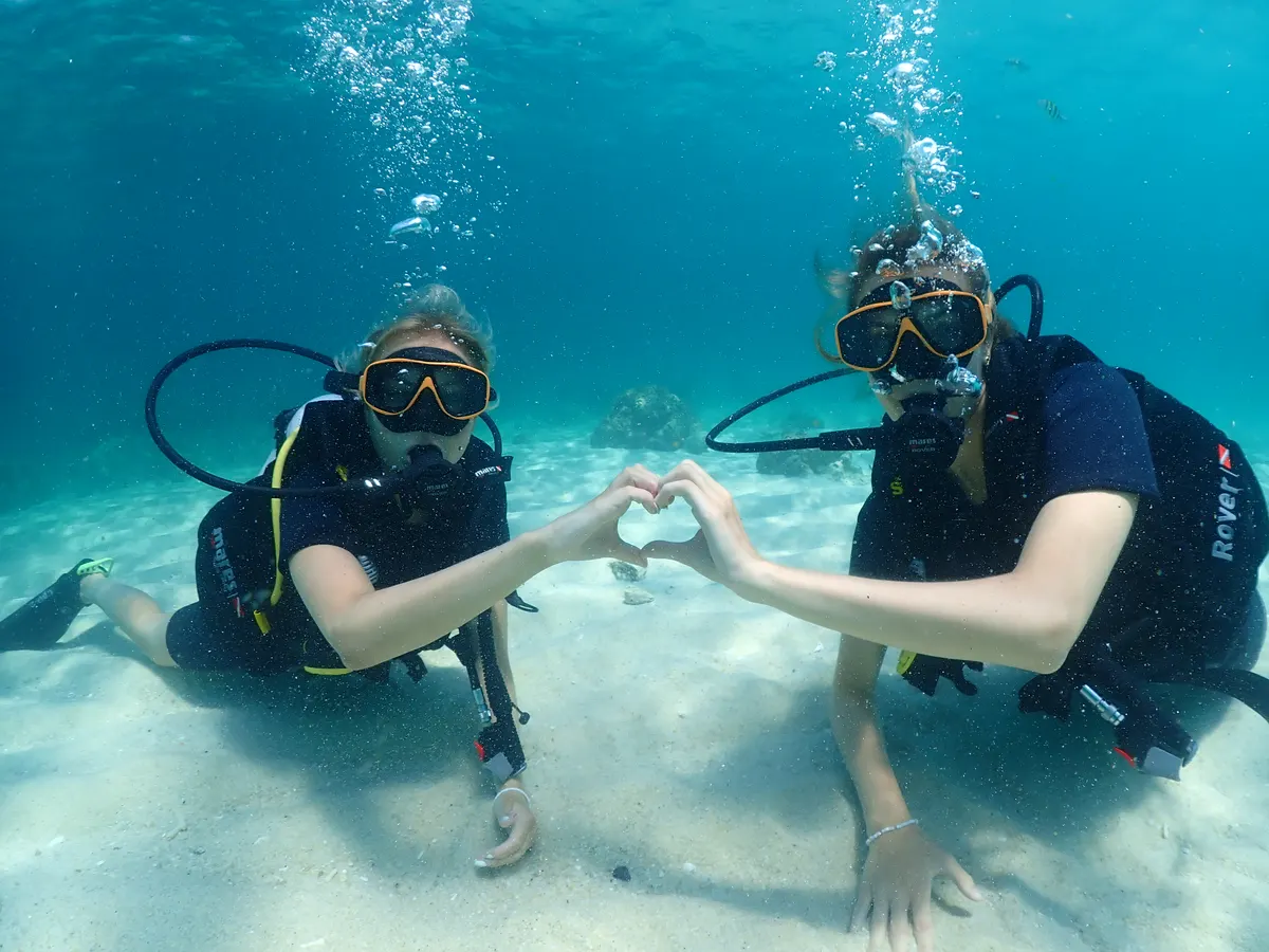 Two divers making a heart over the sandy bottom during the skill session