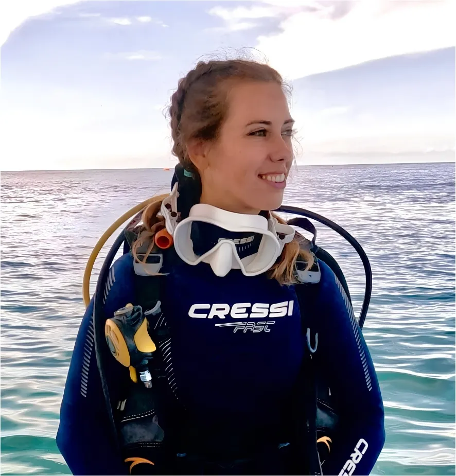 Sara in her dive gear on the boat with the sea behind her