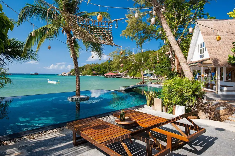 Beachfront bungalows under palm trees on Koh Tao, with a dive boat moored in the calm bay in front