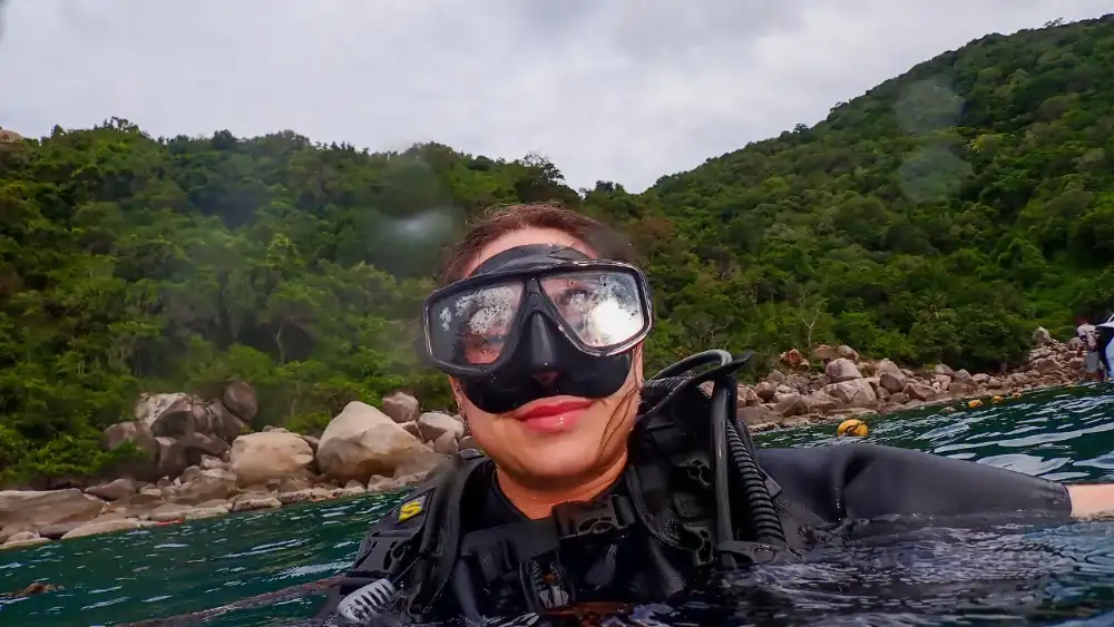 White sand beach on Koh Tao with turquoise water, longtail boats and jungle-covered granite boulders along the shore