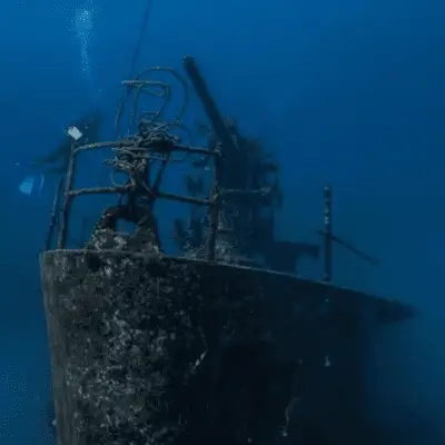 The bow and superstructure of the HTMS Sattakut wreck rising out of the blue, with a diver visible in the background