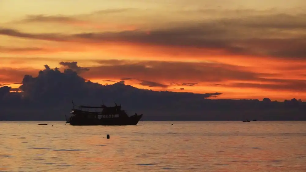 A dive boat anchored off Koh Tao at sunset, dark clouds glowing orange over a calm sea