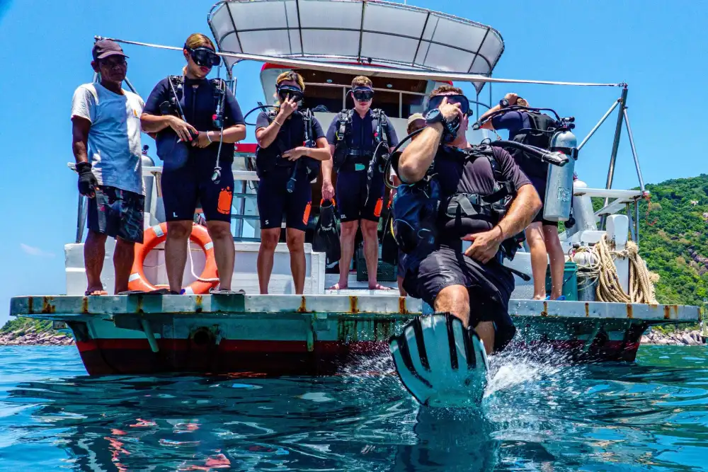 A diver giant-striding off the back of a dive boat in Koh Tao while a line of students in full scuba gear waits on the platform behind