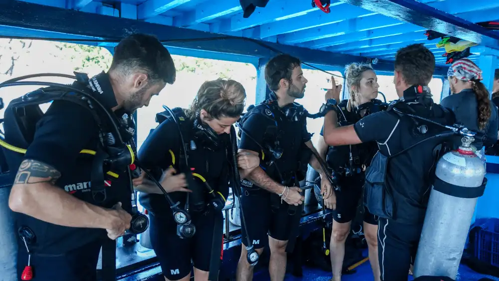 A dive instructor briefing a group of new divers as they gear up on the deck of a dive boat