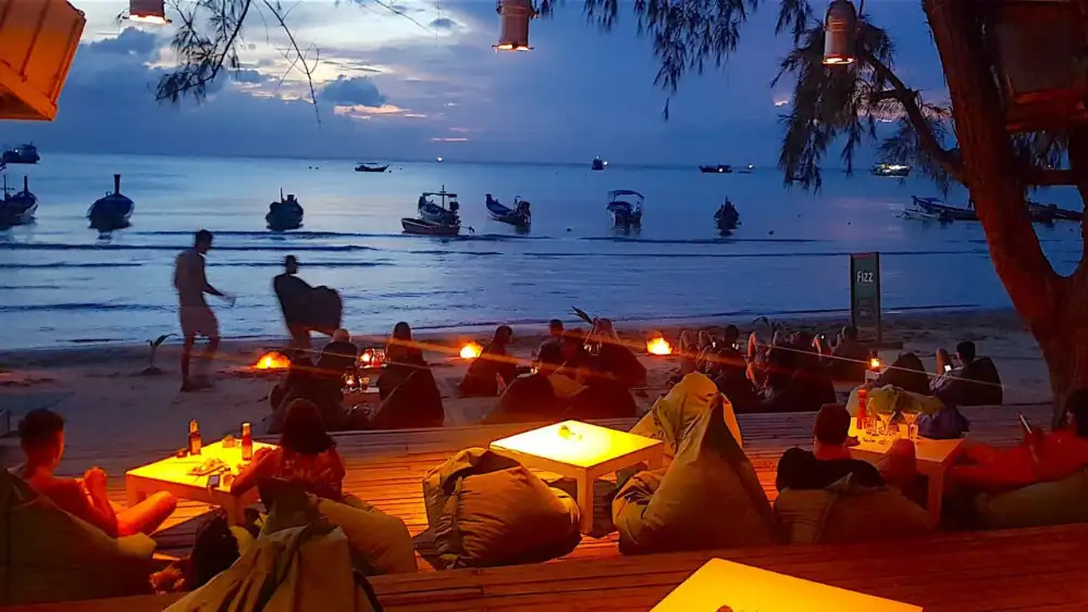 Diners at a beachfront restaurant on Koh Tao with plates of Thai food and the sea behind them