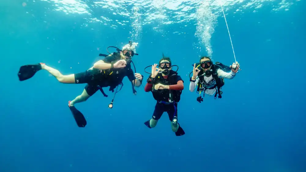 Three scuba divers swimming together underwater during a guided dive in clear water