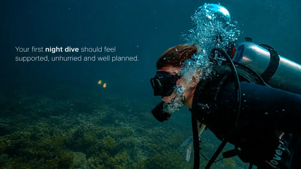 A diver breathing out a stream of bubbles above a dark reef, with the caption: your first night dive should feel supported, unhurried and well planned